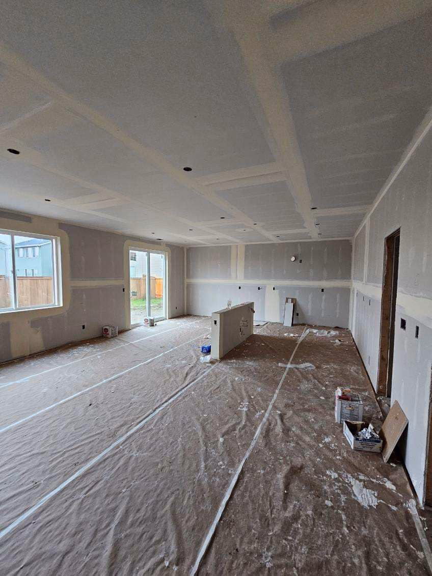 Empty room under construction with drywall walls and ceiling, plastic-covered floor, and a half wall in the center.
