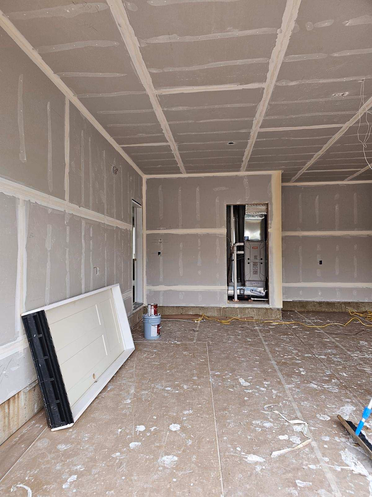 Interior under construction with drywall installed, unpainted door leaning inside, and construction materials on floor.