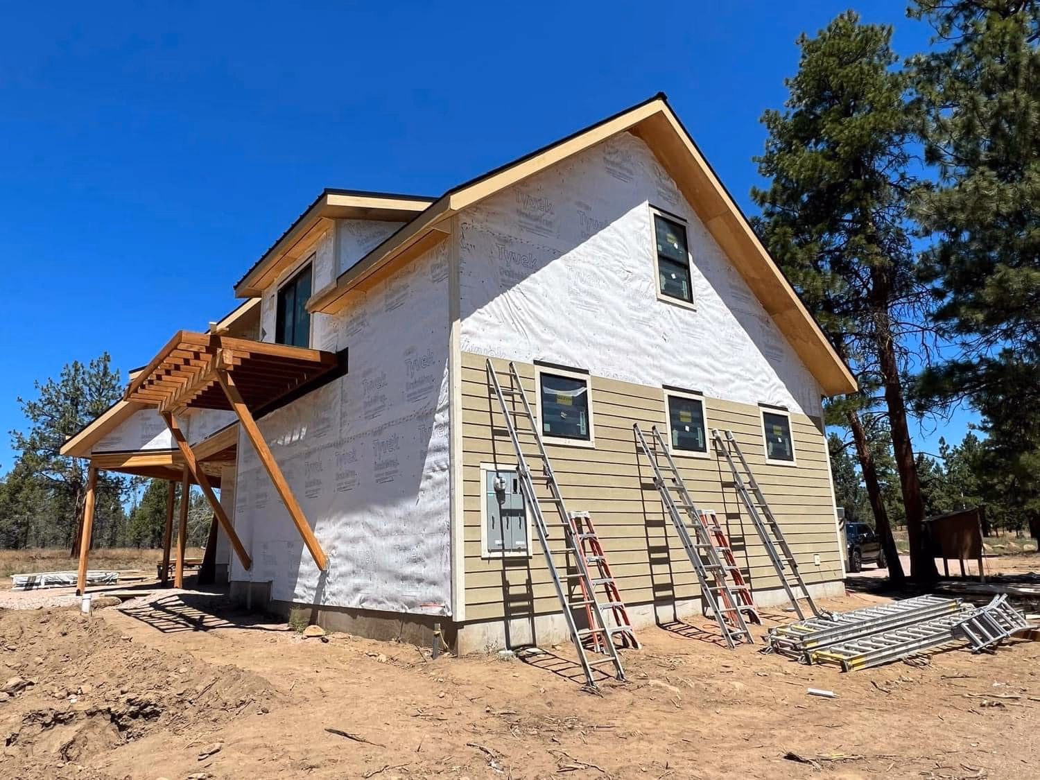 Partially constructed house with siding installed on lower walls and ladders leaning against it outdoors.