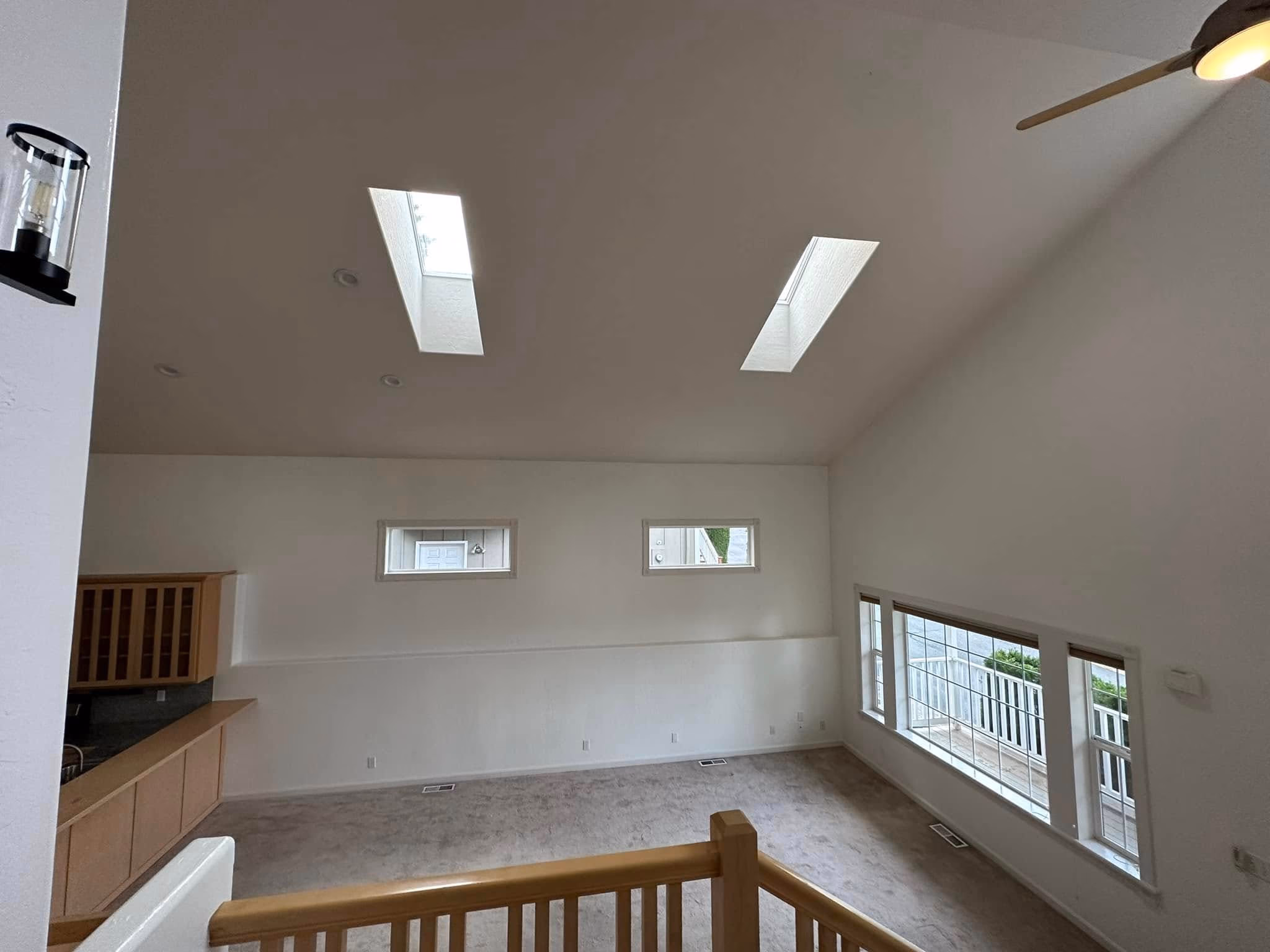 Empty room with carpet, high ceiling, two skylights, small and large windows, and a ceiling fan.