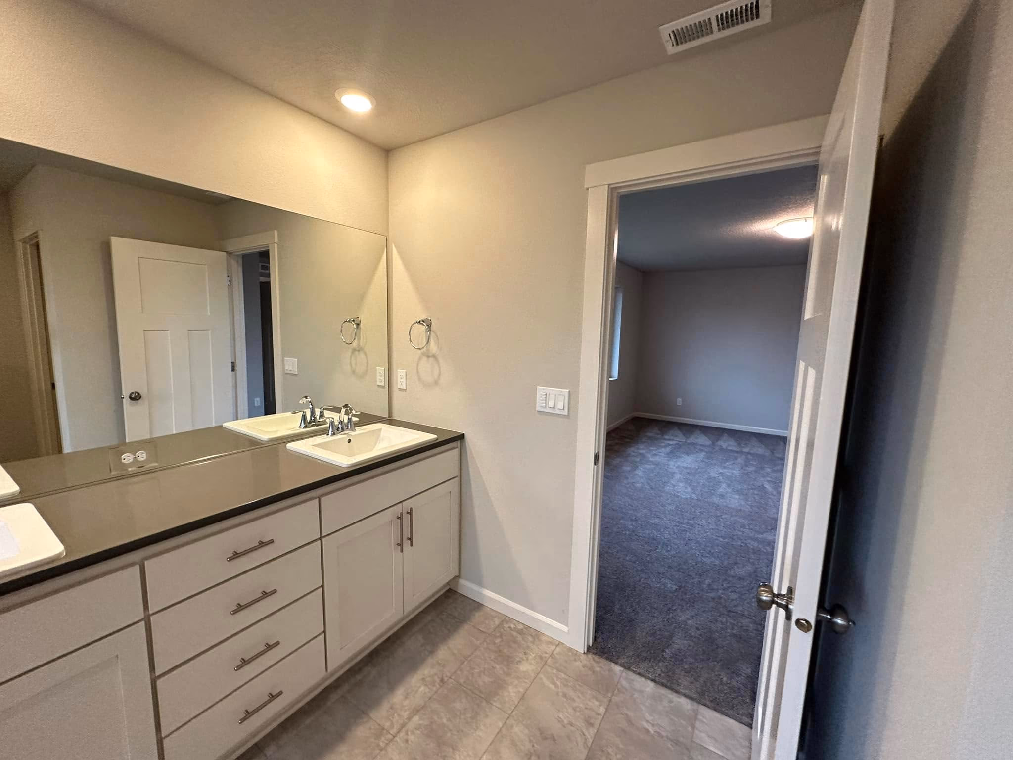 Bathroom with a large mirror, single sink, white cabinets, and an open door leading to a carpeted room.