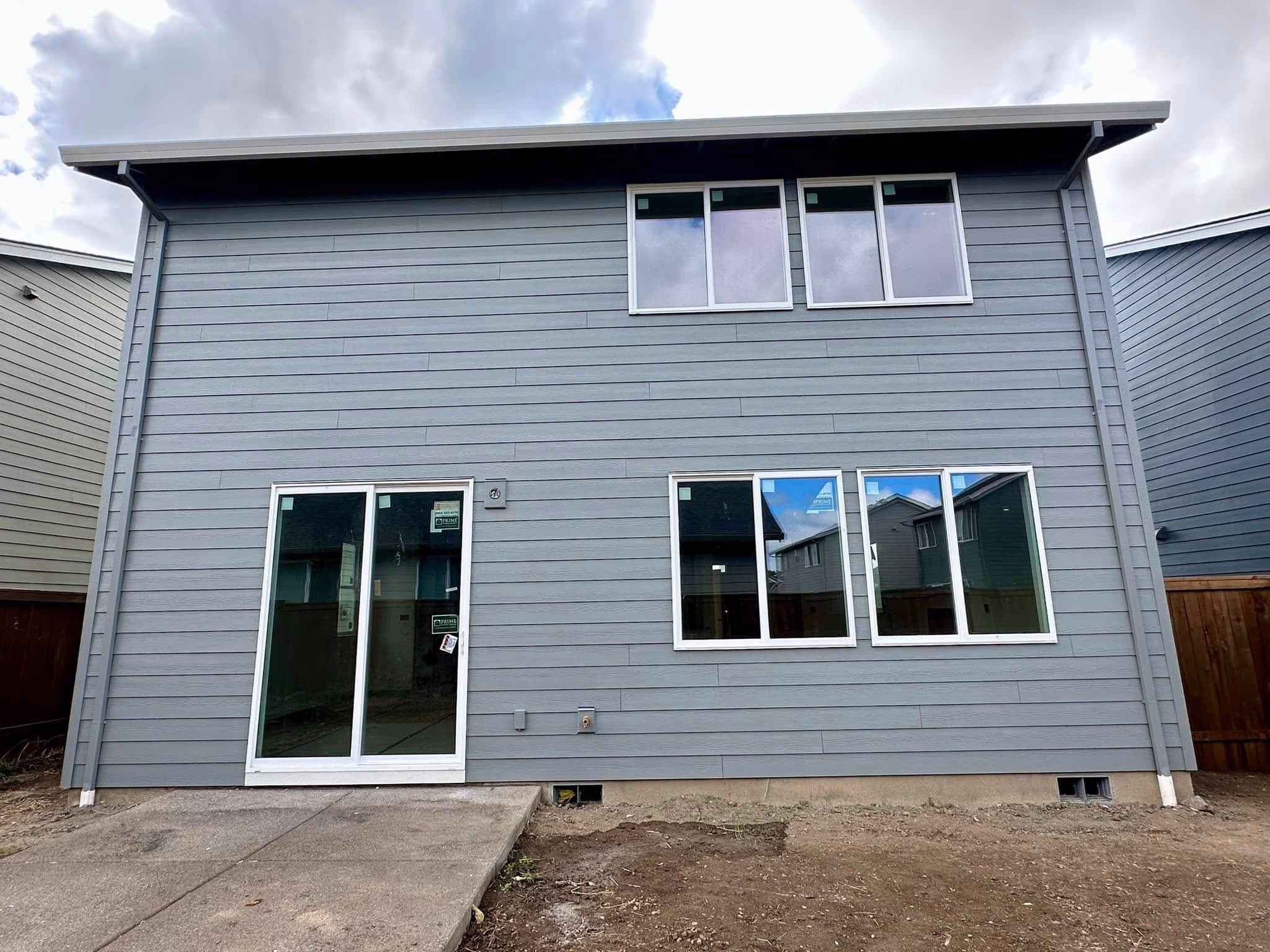 Back of a new two-story gray house with white-framed windows and a sliding glass door.