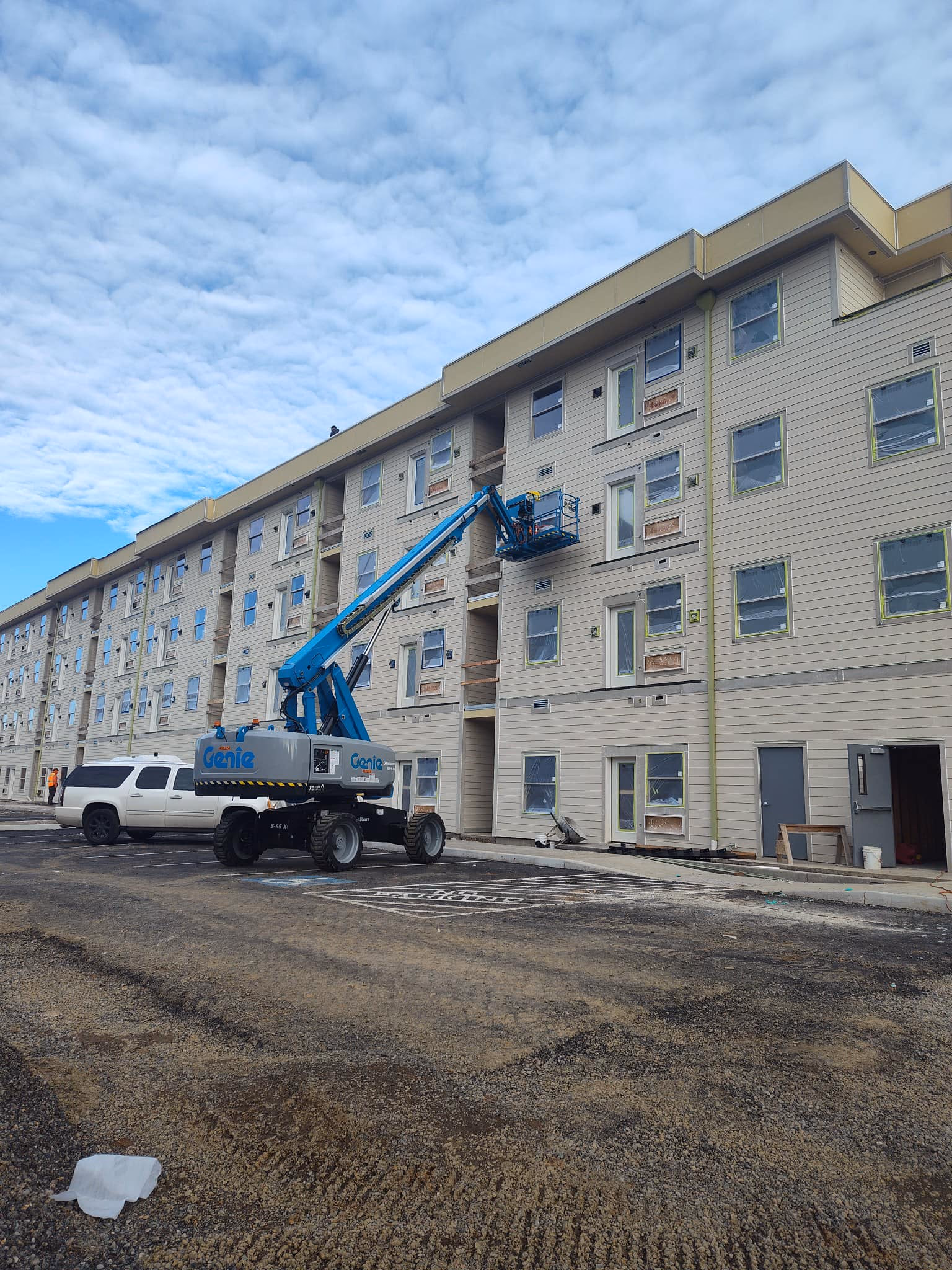 Construction site with a beige multi-story building and a blue Genie lift in front under a cloudy sky.
