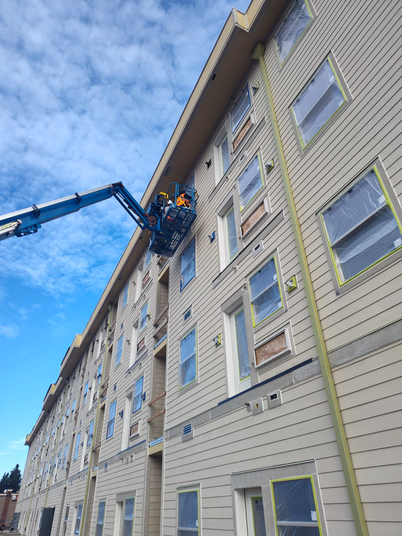 Worker in a lift basket working on the exterior of a large multi-story building under construction.