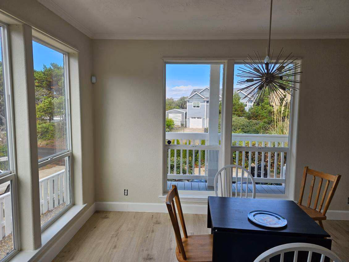 Dining area with black table, wooden and white chairs, large windows, and view of houses outside.