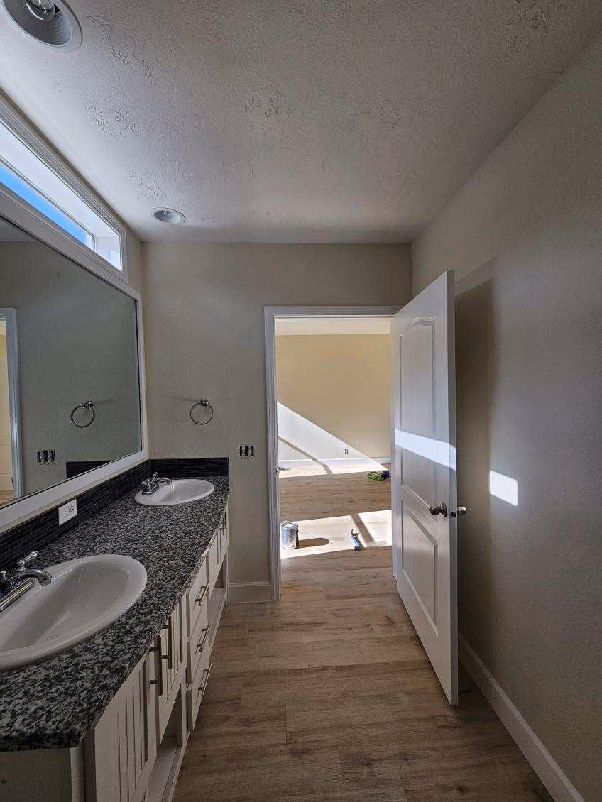 Bathroom with double sinks, granite countertop, and open door leading to sunlit room with paint supplies.