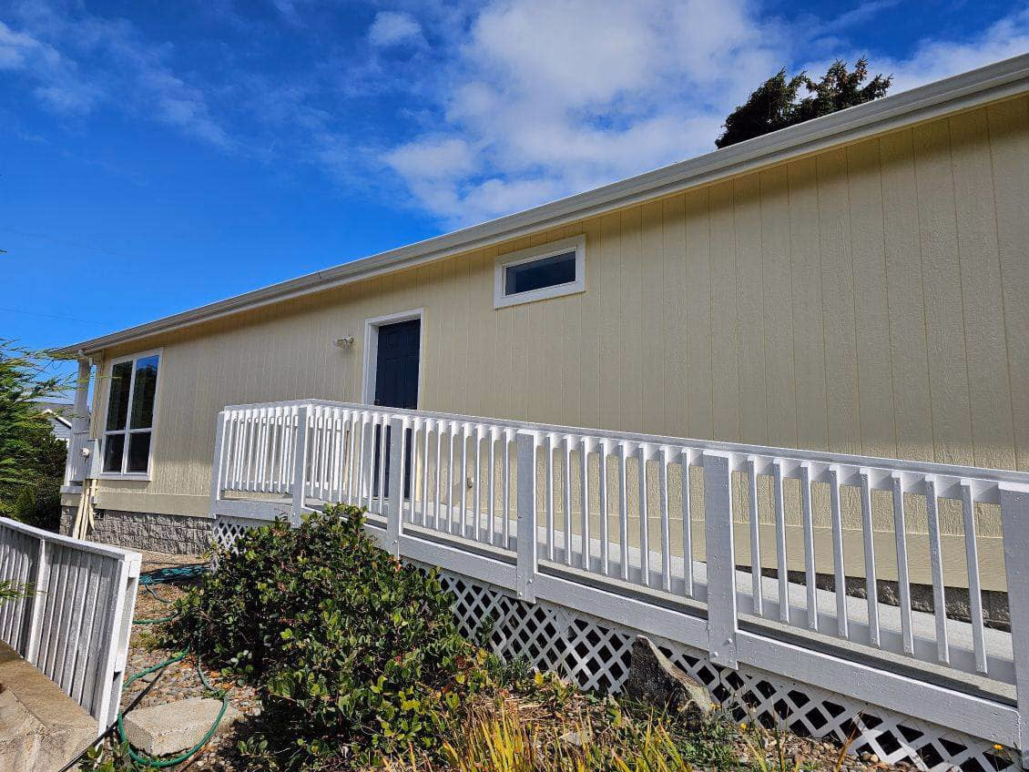 Yellow exterior wall of a building with a white wheelchair ramp and a black door under a blue sky.