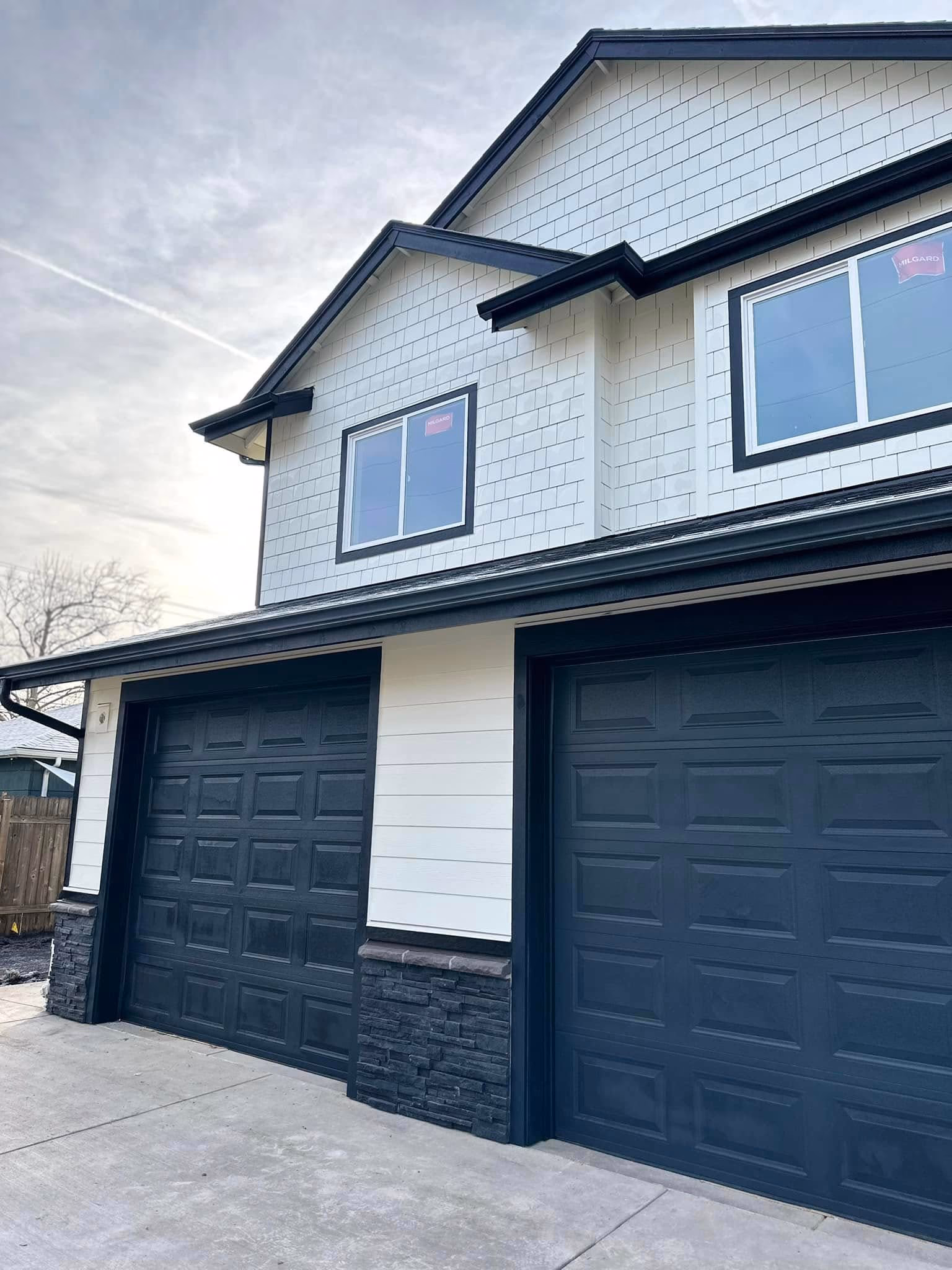 Two closed black garage doors on a white house with black trim and stone accents on the lower walls.