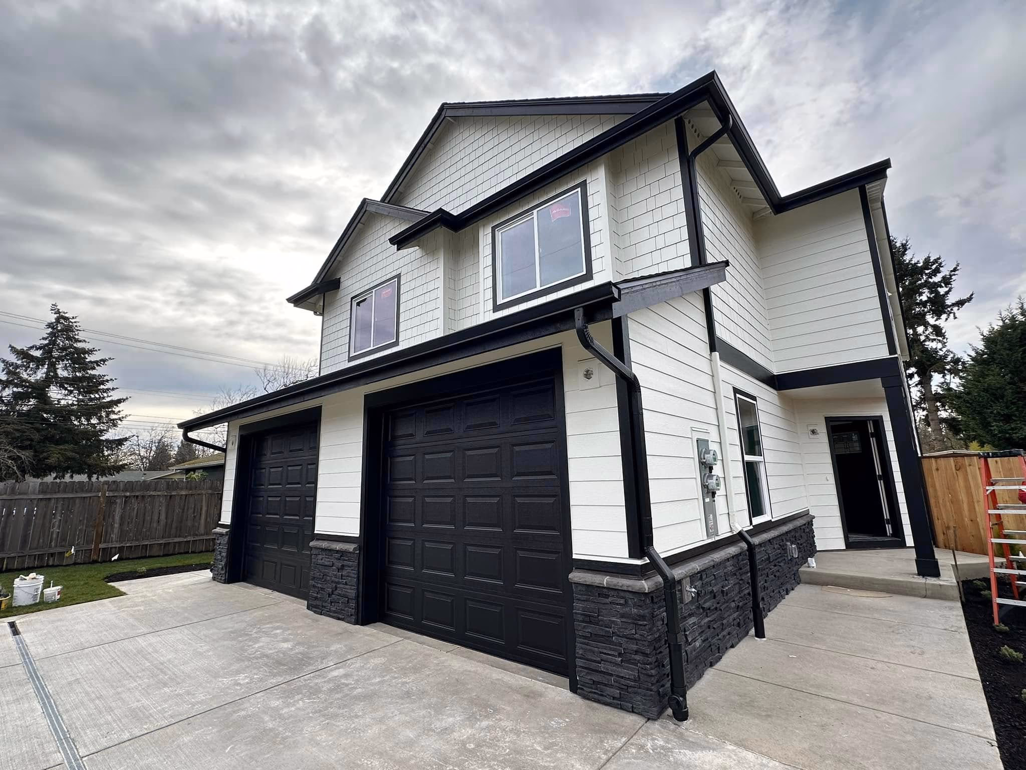 Two-story white house with black trim, black double garage doors, and concrete driveway under a cloudy sky.