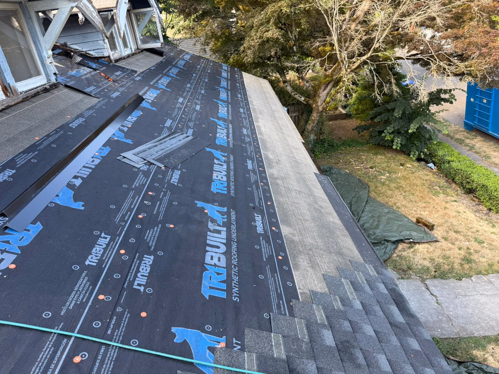 Roof installation showing synthetic roofing underlayment labeled TRIBUILT and partial shingle placement.