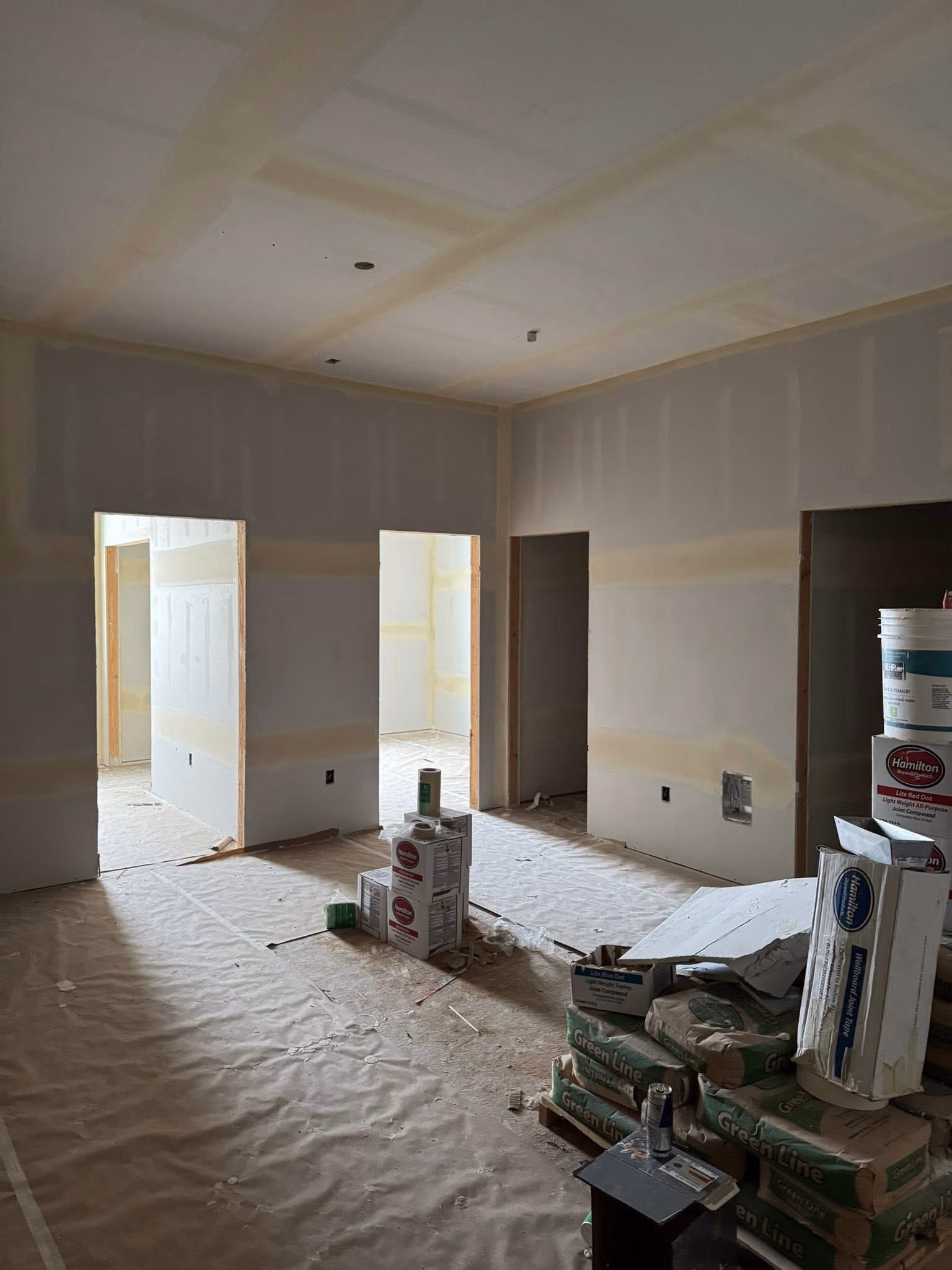 Interior of a room under construction with drywall, stacks of Green Line bags, and paint supply boxes.