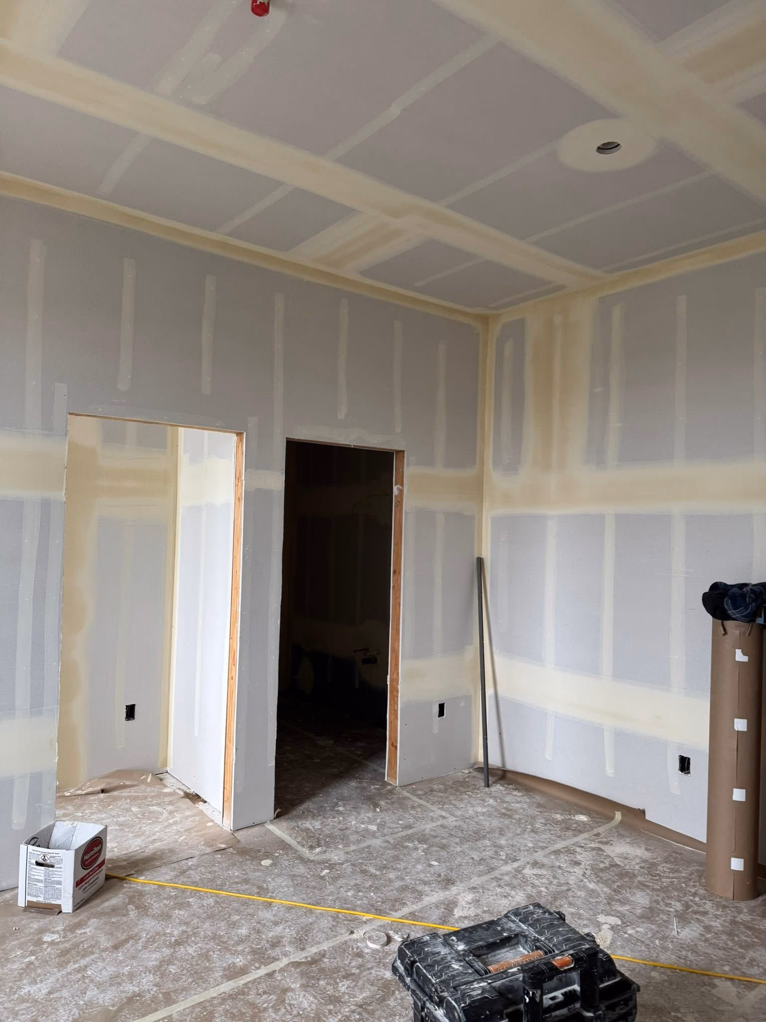 Room under construction with drywall installed, taped seams, two doorways, and construction tools on the floor.