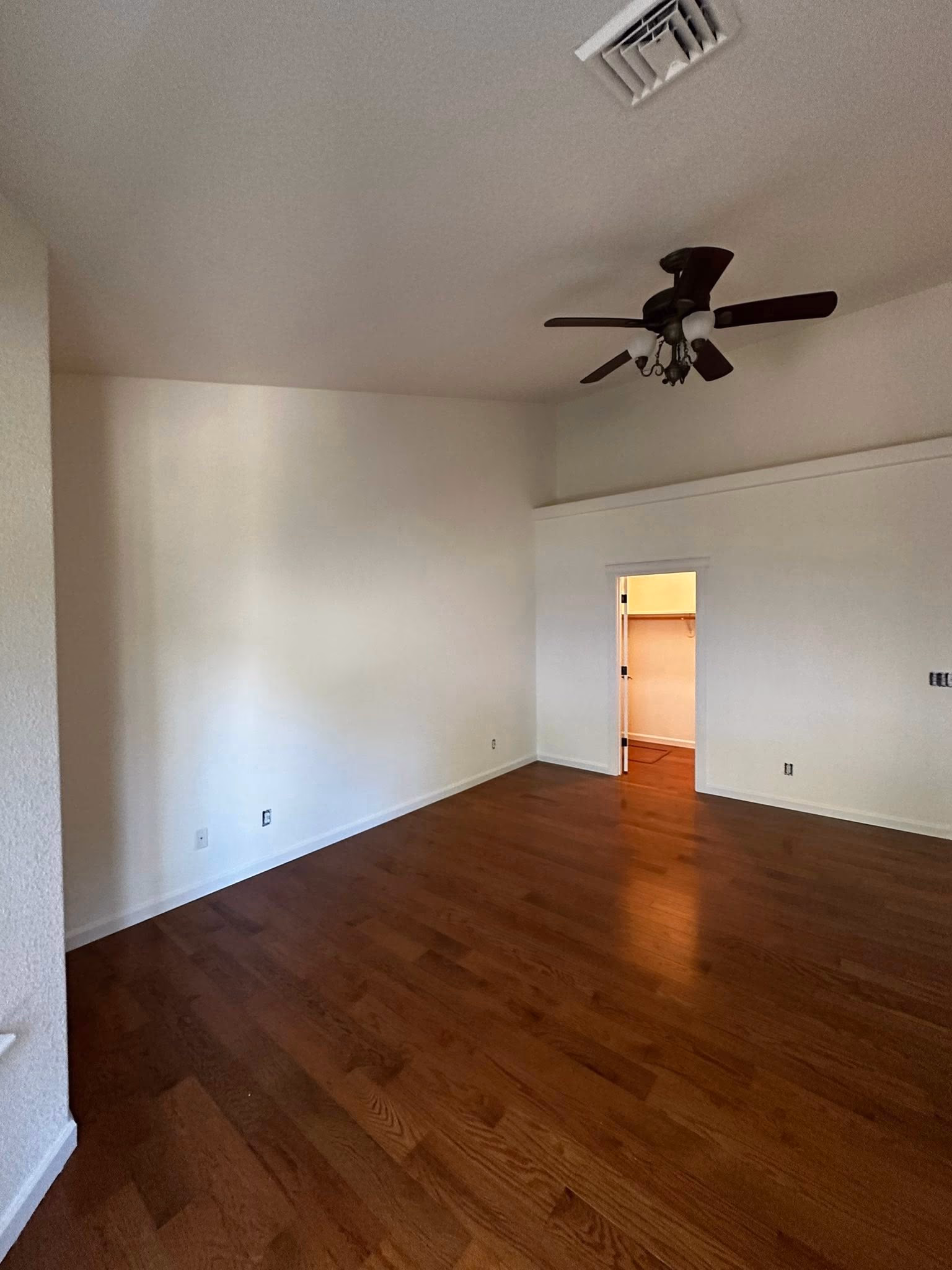 Empty room with wood flooring, white walls, ceiling fan, and open doorway to closet.