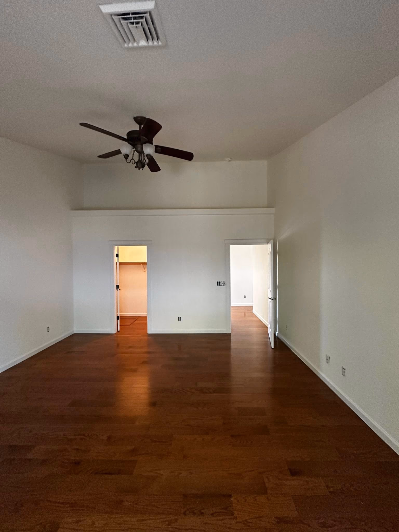 Empty room with dark wooden floor, white walls, ceiling fan, and two open doorways.