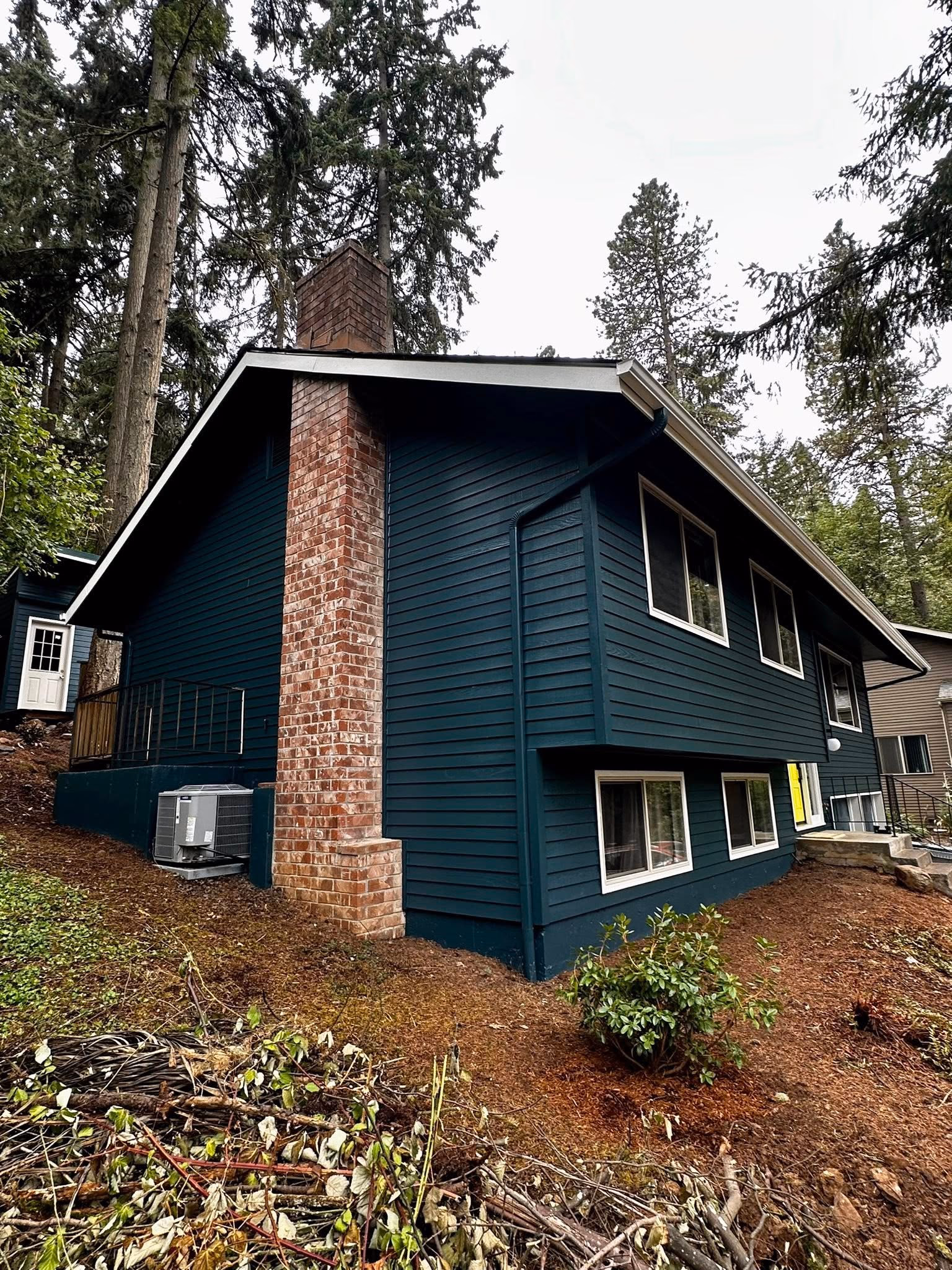 Blue two-story house with white trim and a bright yellow door on a sloped yard with trees.
