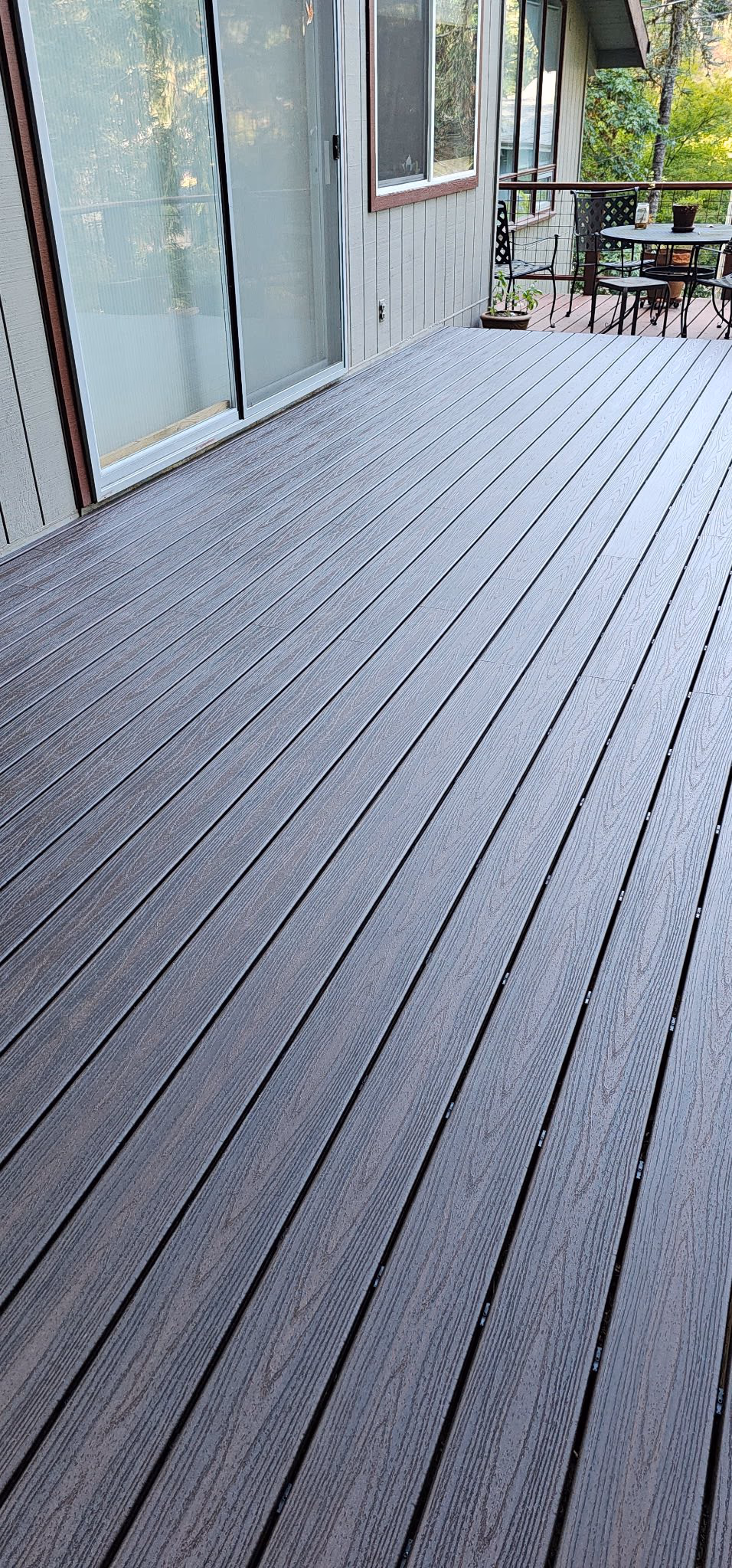Clean gray wooden deck with glass sliding door and outdoor table and chair set in background.