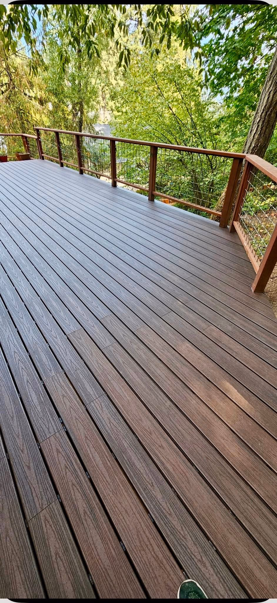 Wooden deck with railing surrounded by green trees.