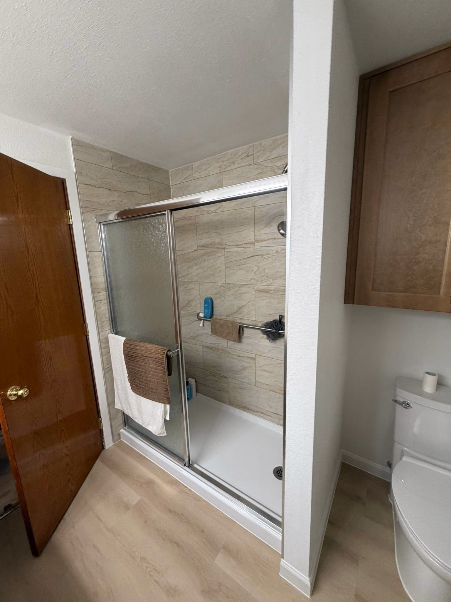 Bathroom with tiled shower enclosure, sliding frosted glass doors, towels hanging, and a white toilet.