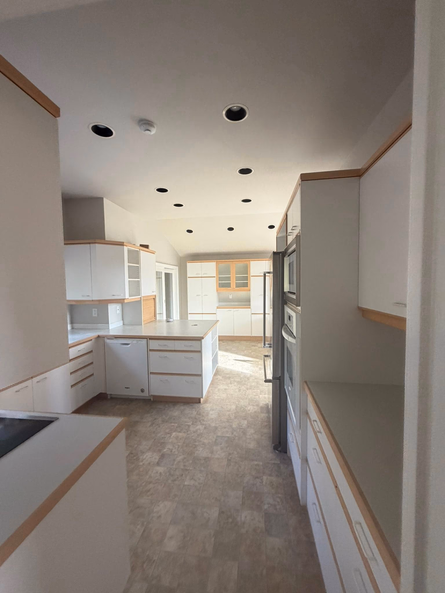 Bright kitchen with white cabinets, wood trim, large island, and tiled floor under recessed ceiling lights.