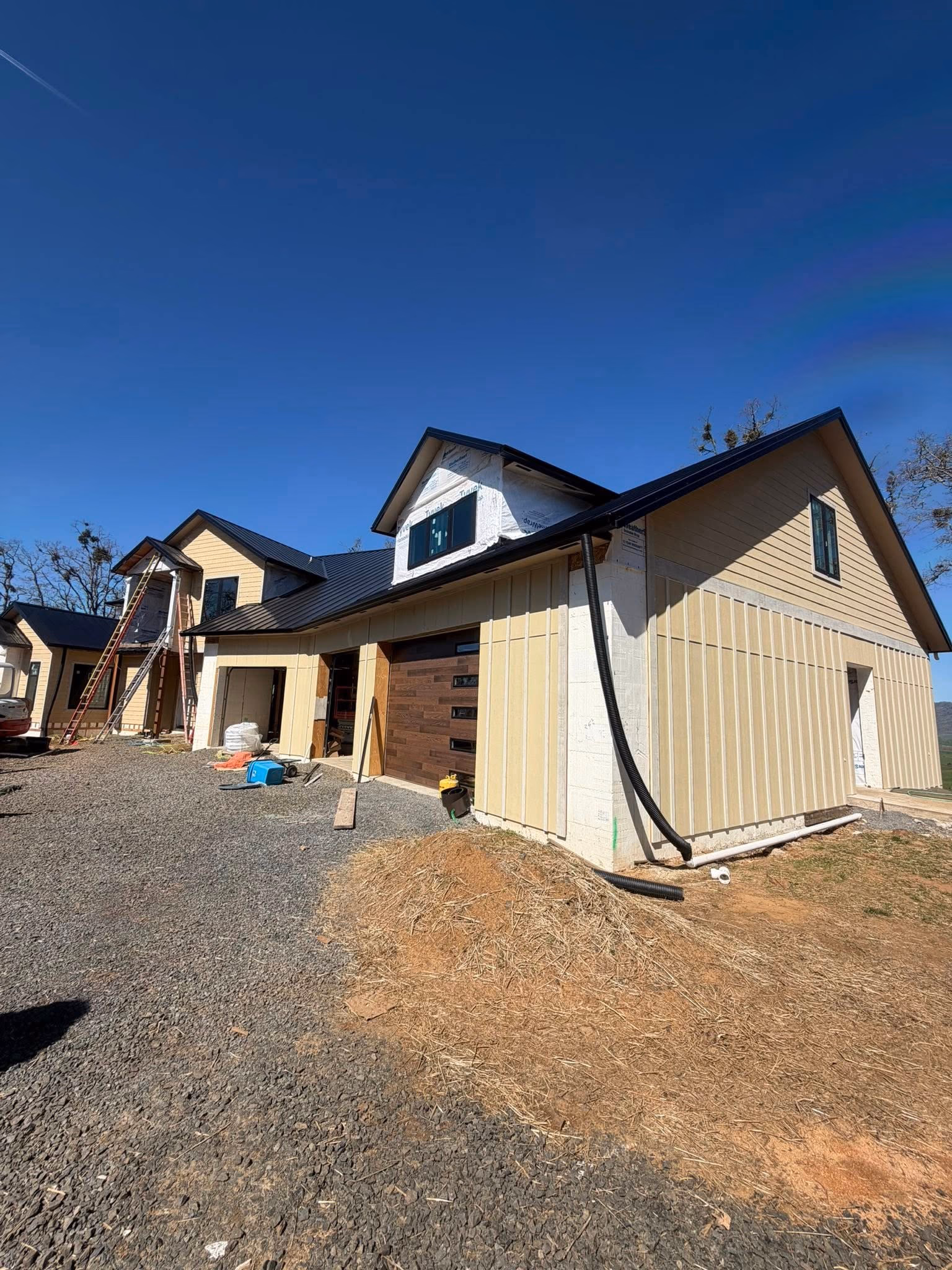 A large house under construction with yellow siding, two dormer windows, and a gravel driveway.