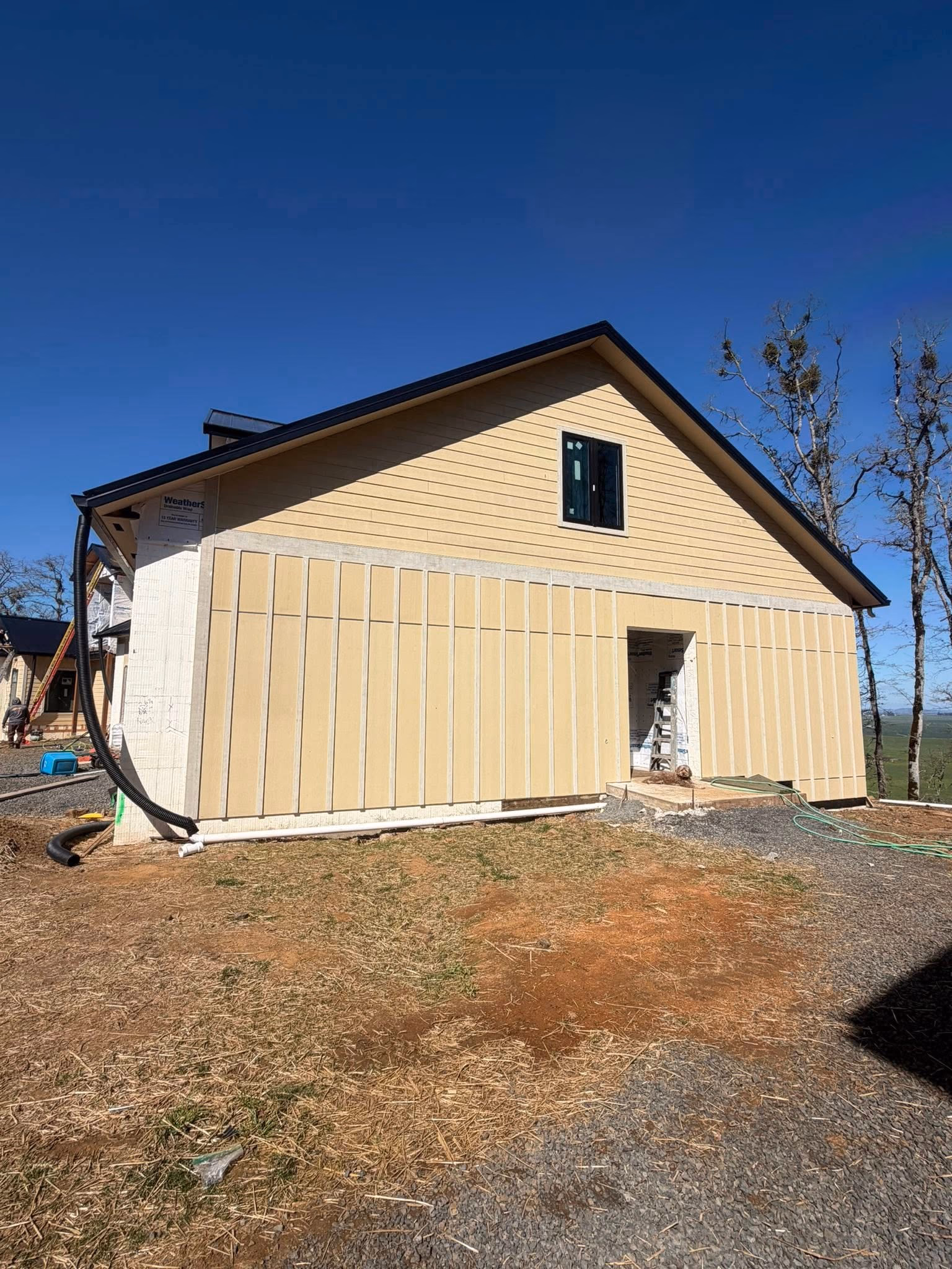 Partially constructed house wall with beige siding and a single window under a clear blue sky.