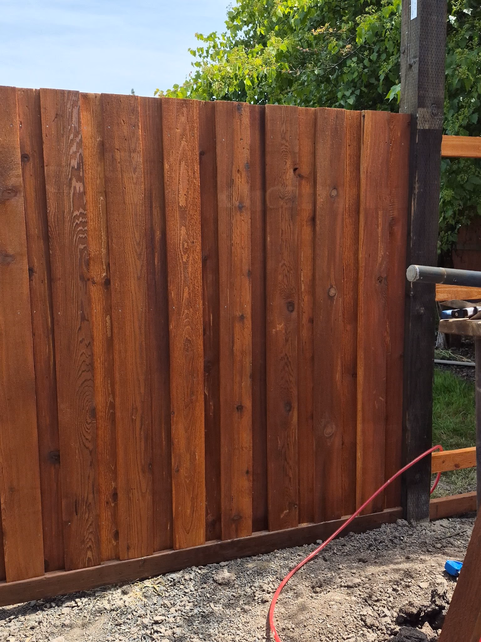 Newly installed wooden fence with vertical planks, gravel ground, and garden greenery in the background.