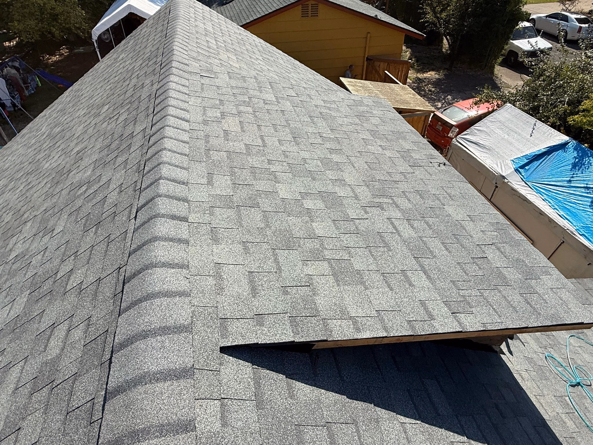 Close-up aerial view of a gray shingled roof with a vent and nearby parked cars and tents.