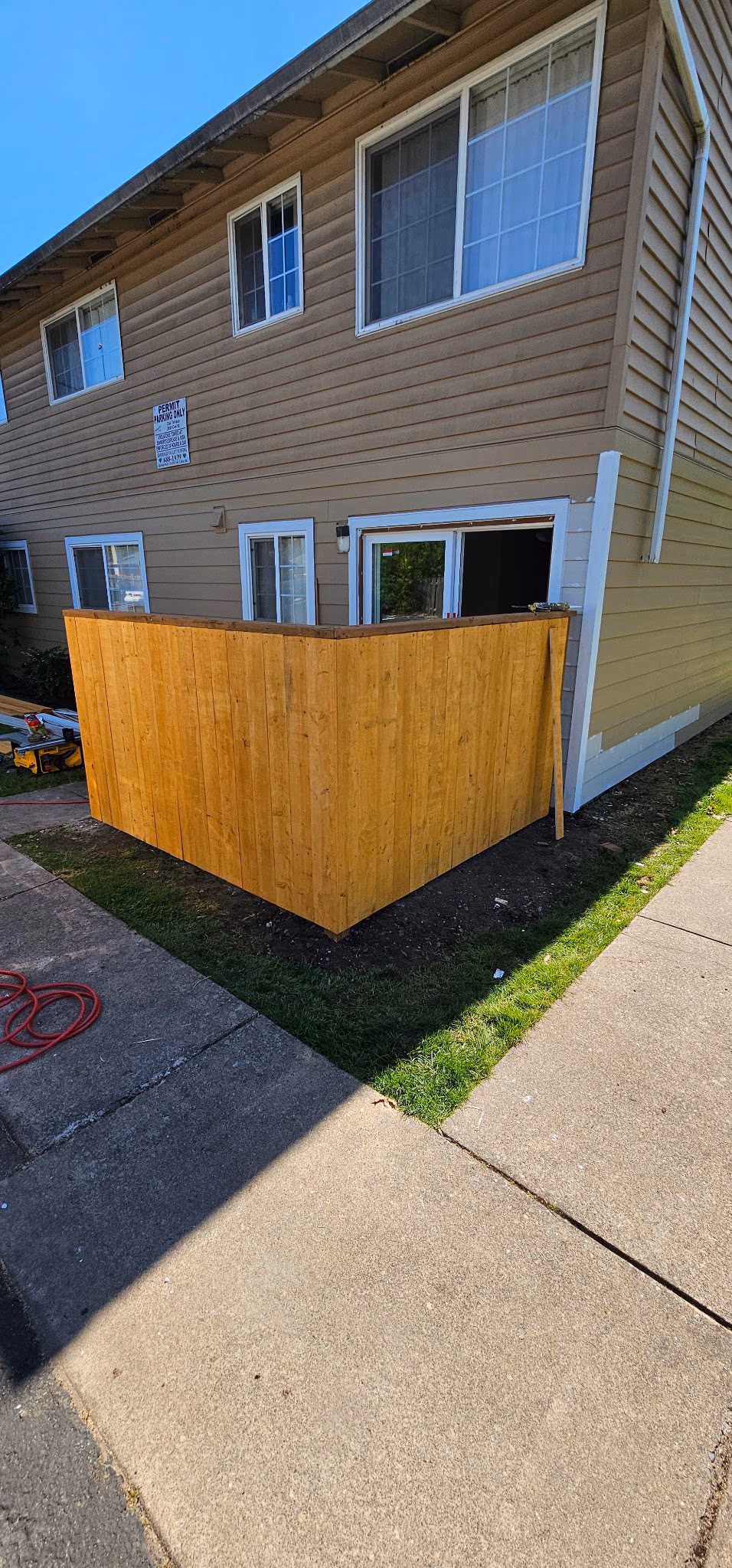 New wooden privacy fence enclosing a ground-level patio of a beige residential building.