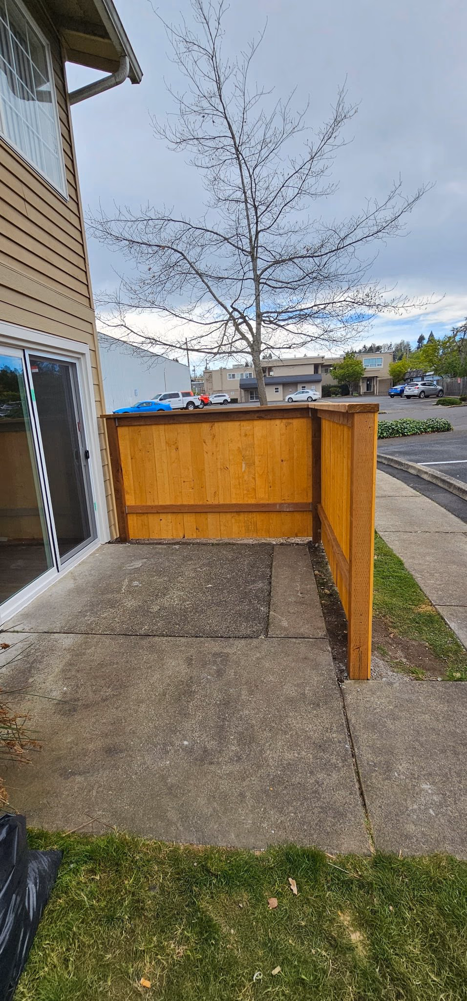 Concrete patio with orange wooden privacy fence, adjacent to house with sliding glass door and leafless tree.