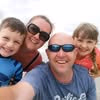 Smiling man wearing sunglasses with two children and another man outdoors close together.